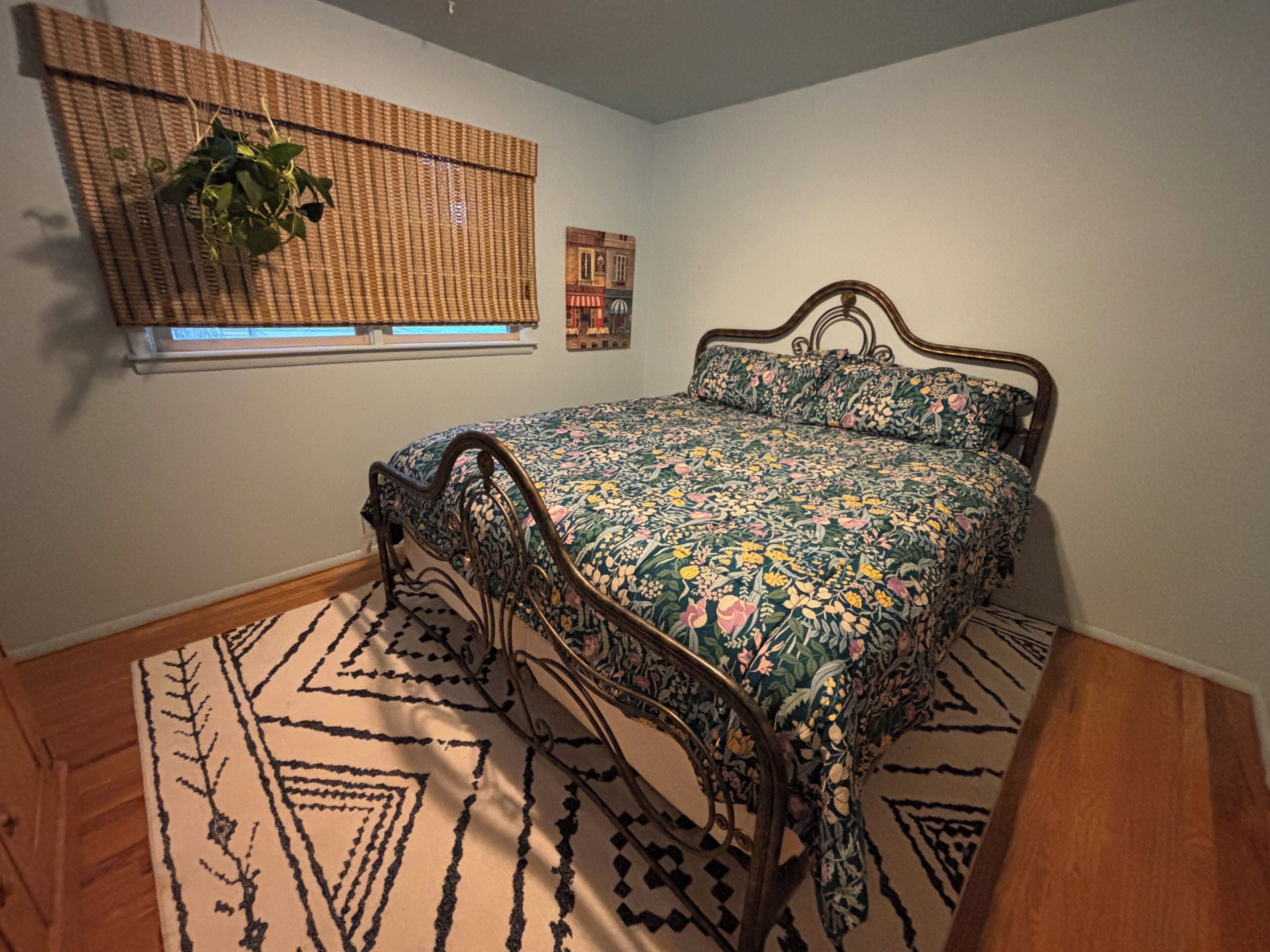 A bedroom with a bed, a window with a plant, and a wall decoration.