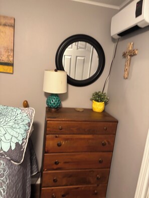 A bedroom with a bed, a dresser, a mirror, a lamp, a small plant, and a wall-mounted air conditioner. - Lake Front Sleeps 4.  Close to Waterfalls, Parks, Golf, Fishing & Dog Friendly (Crossville)