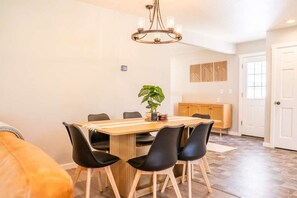 Comedor con mesa de madera, sillas negras, una lámpara de araña y una planta en maceta.