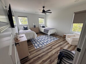 Une chambre avec deux lits, un ventilateur de plafond, un plancher en bois et une fenêtre.