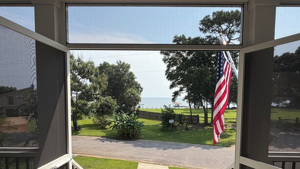 Vista desde una ventana sobre un área verde con una bandera, un sendero y una masa de agua.