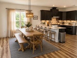 A modern kitchen with dark cabinets, a central island, and a dining area with wooden chairs and a bench. - Paradise Beach on Perdido Bay• Dog Friendly (Pensacola)