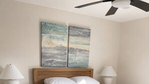 Un dormitorio con una cama de madera, dos mesitas de noche con lámparas, un tapete estampado y dos cuadros en la pared.