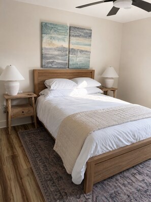 A bedroom with a wooden bed, two bedside tables with lamps, a patterned rug, and two wall art pieces. - Paradise Beach on Perdido Bay• Dog Friendly (Pensacola)