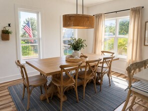 A dining area with a wooden table and chairs, a hanging light fixture, and a view of the outdoors.