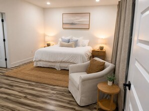 A bedroom with a bed, bedside tables, a chair, a rug, and a painting on the wall.