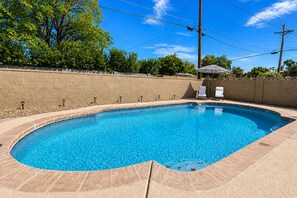 Ein rechteckiger Pool mit Fliesenrand, umgeben von einer Ziegelmauer und einer Holzterrasse.