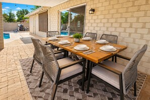 An outdoor dining area with a brick wall, a pool, and a covered patio. - Aloha Scottsdale, Poolside Old Town Retreat (Scottsdale)