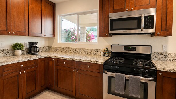 A kitchen with wooden cabinets, a stainless steel stove, a microwave, and a window with a view of flowers. - Aloha Scottsdale, Poolside Old Town Retreat (Scottsdale)