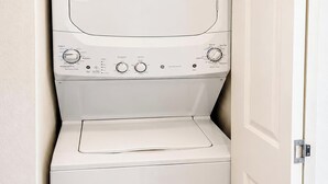 A white, compact washer and dryer unit with control knobs and a door, installed in a corner of a room. - Aloha Scottsdale, Poolside Old Town Retreat (Scottsdale)