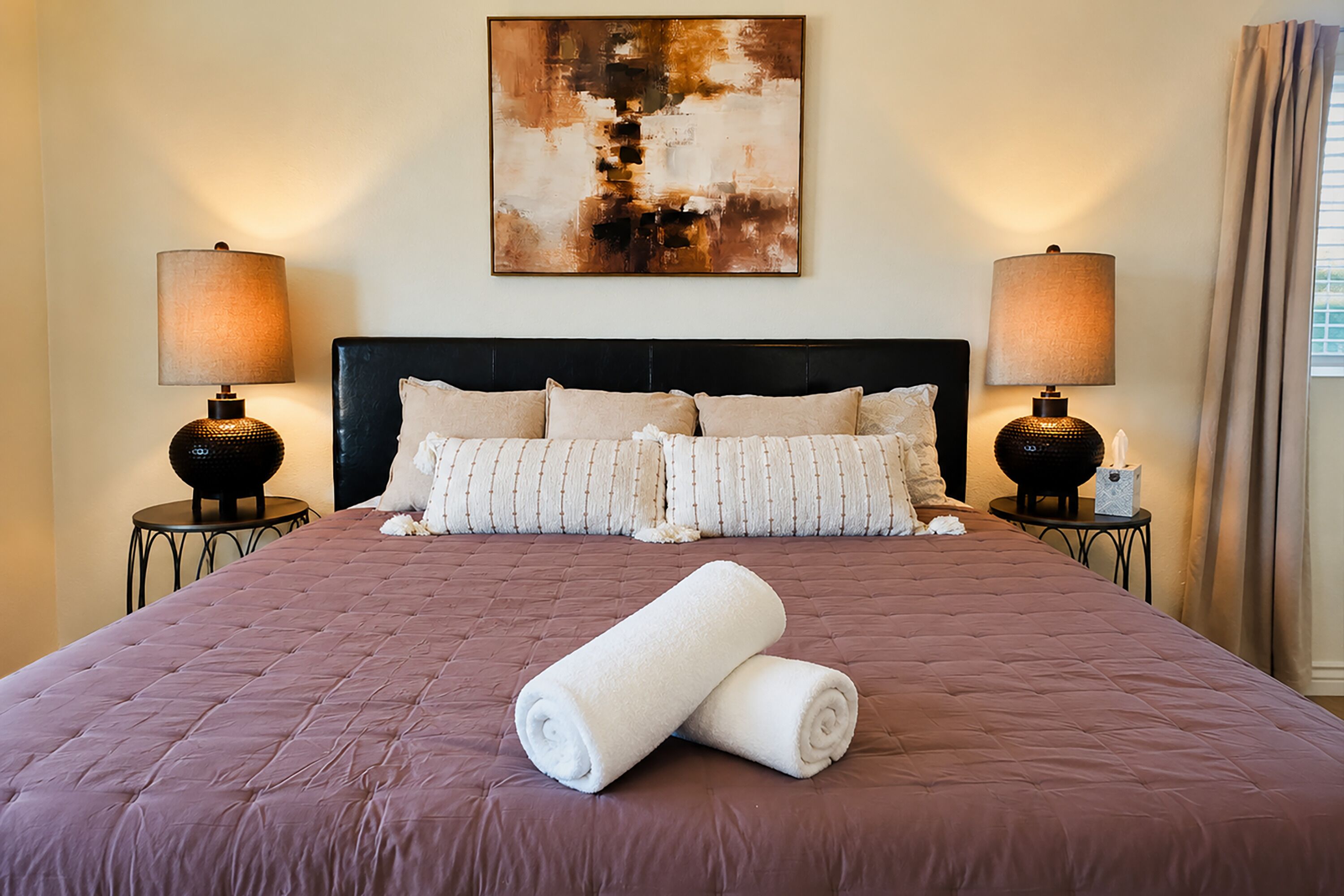A hotel room with a large bed, two bedside lamps, a headboard, and a painting on the wall.