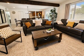 Ein Wohnzimmer mit einer dunkelbraunen Ledersofa-Garnitur, einem Couchtisch und einem Essbereich im Hintergrund.