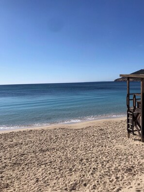 A beach with clear blue water, a sandy shore, and a wooden structure.