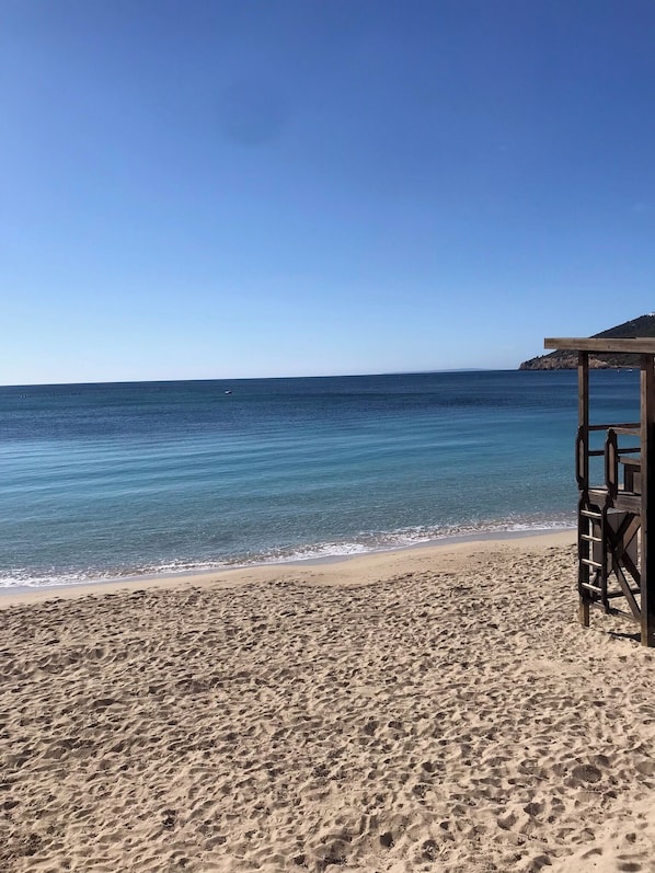 A beach with clear blue water, a sandy shore, and a wooden structure.