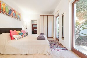 A bedroom with a large bed, a colorful artwork, a sliding door, and a view of the outdoors.