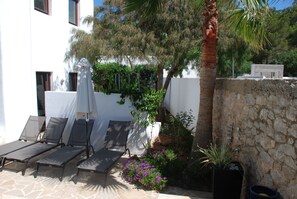Ein sonniger Außenbereich mit Sitzgelegenheiten, Lounge-Stühlen und einem Tisch, umgeben von Bepflanzung und einer Steinmauer.