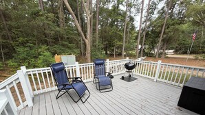 A deck with two chairs and a grill, surrounded by a white fence and trees. - Nonna's Cottage,Spacious 3-bedroom Stand alone house,cart and landtrans included (Daufuskie Island)