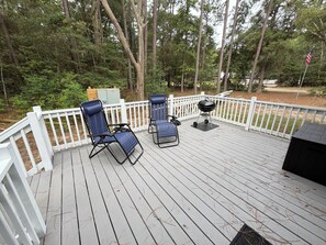 Eine Terrasse mit zwei Stühlen und einem Grill, umgeben von einem weißen Zaun und Bäumen.