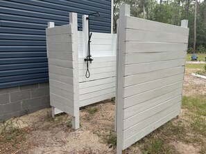 A white wooden gate with a showerhead attached, standing on a sandy ground with grass patches. - Nonna's Cottage,Spacious 3-bedroom Stand alone house,cart and landtrans included (Daufuskie Island)