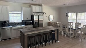 A modern kitchen with a central island, bar stools, and a dining area with white chairs. - Nonna's Cottage,Spacious 3-bedroom Stand alone house,cart and landtrans included (Daufuskie Island)