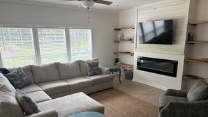 A living room with a sofa, armchair, TV, fireplace, and shelves. - Nonna's Cottage,Spacious 3-bedroom Stand alone house,cart and landtrans included (Daufuskie Island)