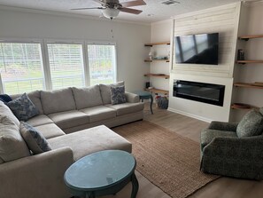 Ein Wohnzimmer mit Sofa, Sessel, Fernseher, Kamin und Regalen.