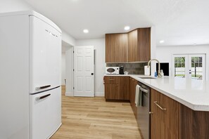 Eine moderne Küche mit einem weißen Kühlschrank, Holzschränken, einer Mikrowelle und einer Spüle aus Edelstahl.