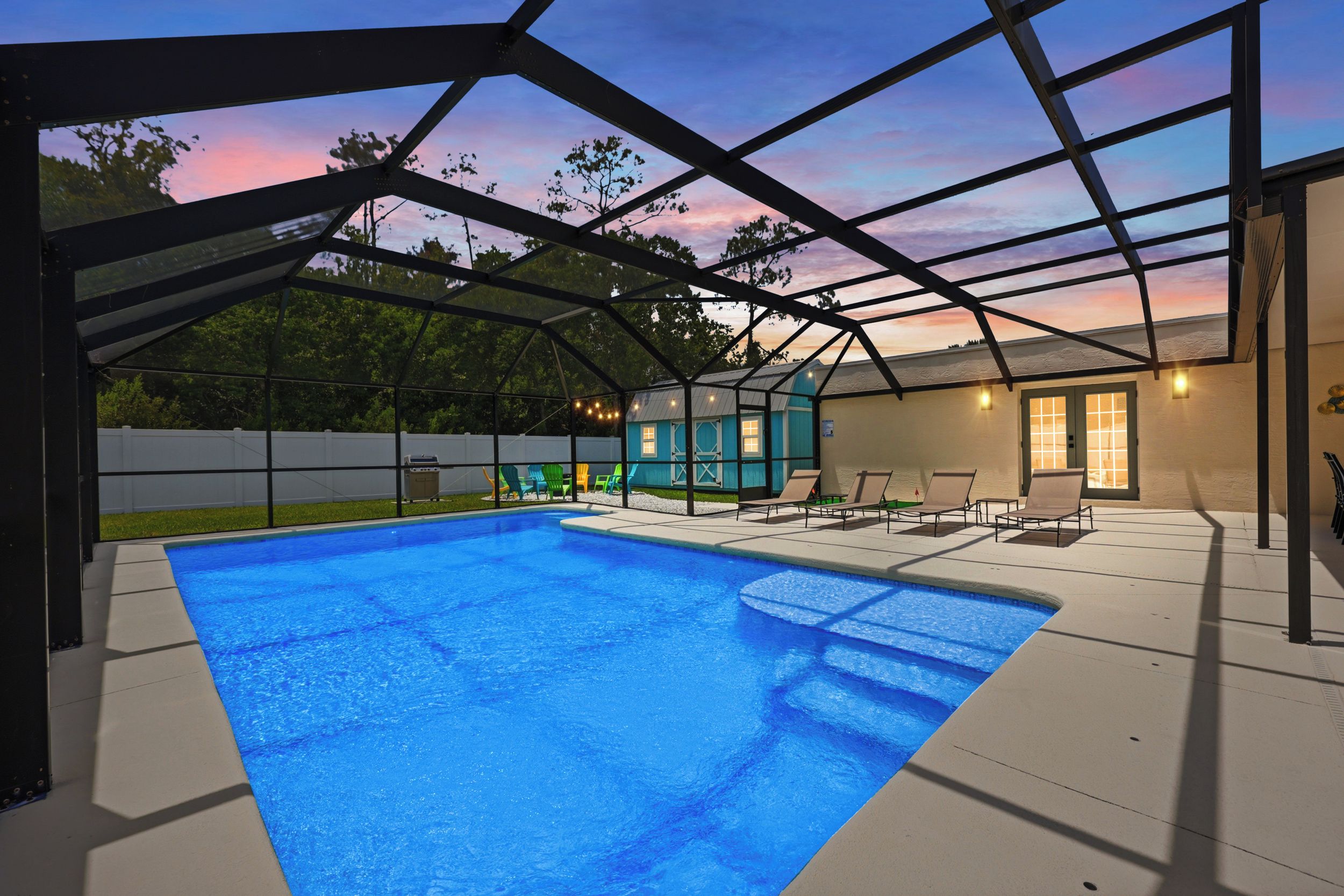 Una piscina techada con vista al atardecer, mobiliario exterior y un edificio pequeño.