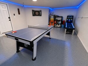A ping pong table with a 'National Hockey League' logo, a dartboard, and a claw machine in a room with blue LED lighting. - 7BR Heated Pool | Game Room + Private Suite (Palm Coast)