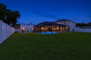 Una casa con piscina techada, patio trasero cercado y luces colgantes.