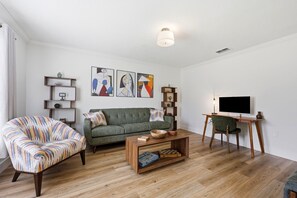 A living room with a green sofa, a patterned armchair, a wooden coffee table, and a television on a stand. - 7BR Heated Pool | Game Room + Private Suite (Palm Coast)