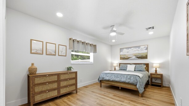 Quarto com cama, penteadeira, ventoinha no teto, obras de arte e janela com cortinas.