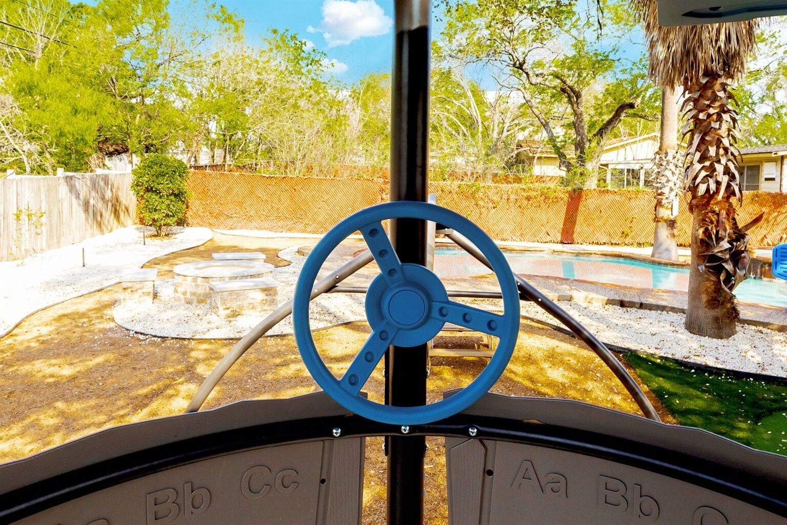A steering wheel with letters indicating controls, a palm tree, and a fenced outdoor area with a pool.