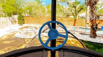 A steering wheel with letters indicating controls, a palm tree, and a fenced outdoor area with a pool.