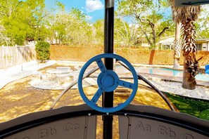 Volante con letras que indican controles, una palmera y un área exterior cercada con piscina.