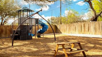 A playground with a slide, swings, and a wooden bench.
