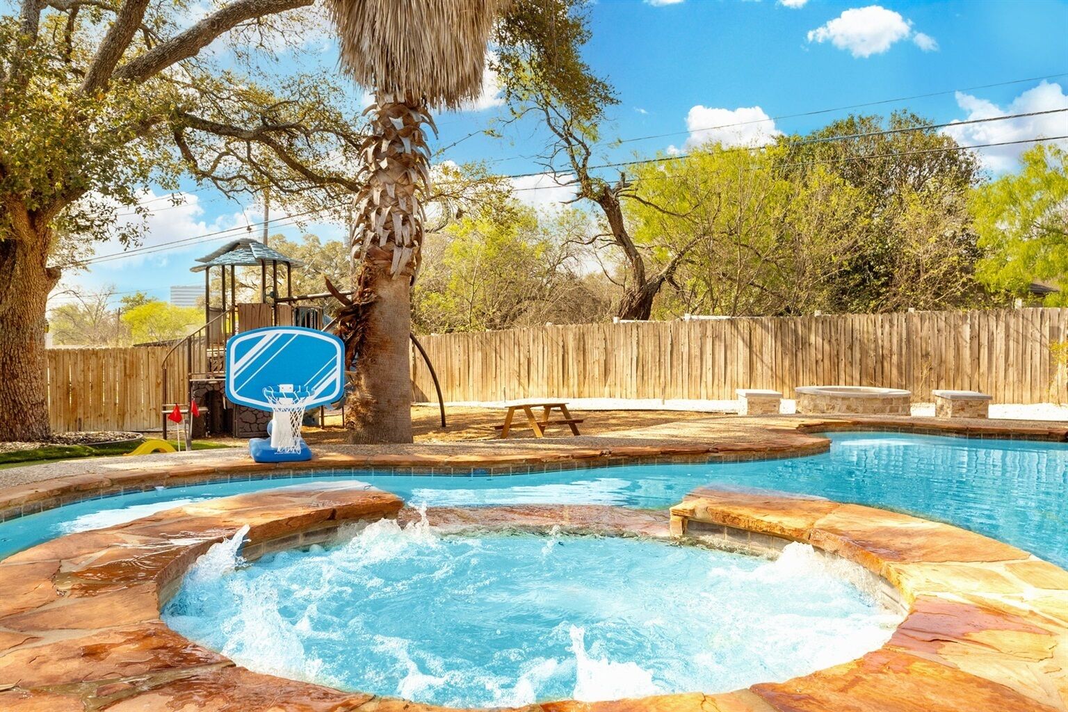 Un patio trasero con piscina, jacuzzi y canasta de baloncesto.