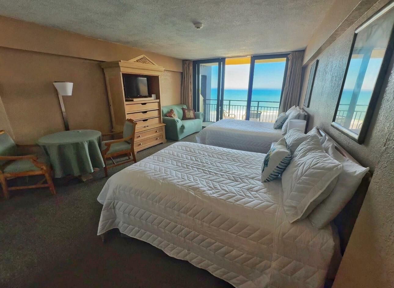 A hotel room with a large bed, a desk, a chair, and a view of the ocean.