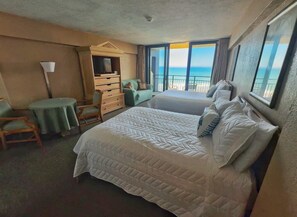 A hotel room with a large bed, a desk, a chair, and a view of the ocean. - NEW Amazing Ocean Front Studio-Up to 4 Guests! (Daytona Beach Shores)
