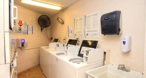 A laundry room with multiple washing machines, a fan, a paper dispenser, and a hand soap dispenser. - NEW Amazing Ocean Front Studio-Up to 4 Guests! (Daytona Beach Shores)