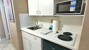 Een kleine keuken met witte kastjes, een magnetron, een spoelbak en een vaatwasser.