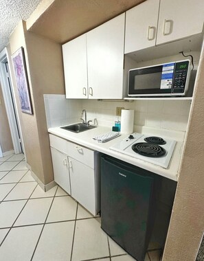 A compact kitchen with white cabinets, a microwave, a sink, and a dishwasher. - NEW Amazing Ocean Front Studio-Up to 4 Guests! (Daytona Beach Shores)