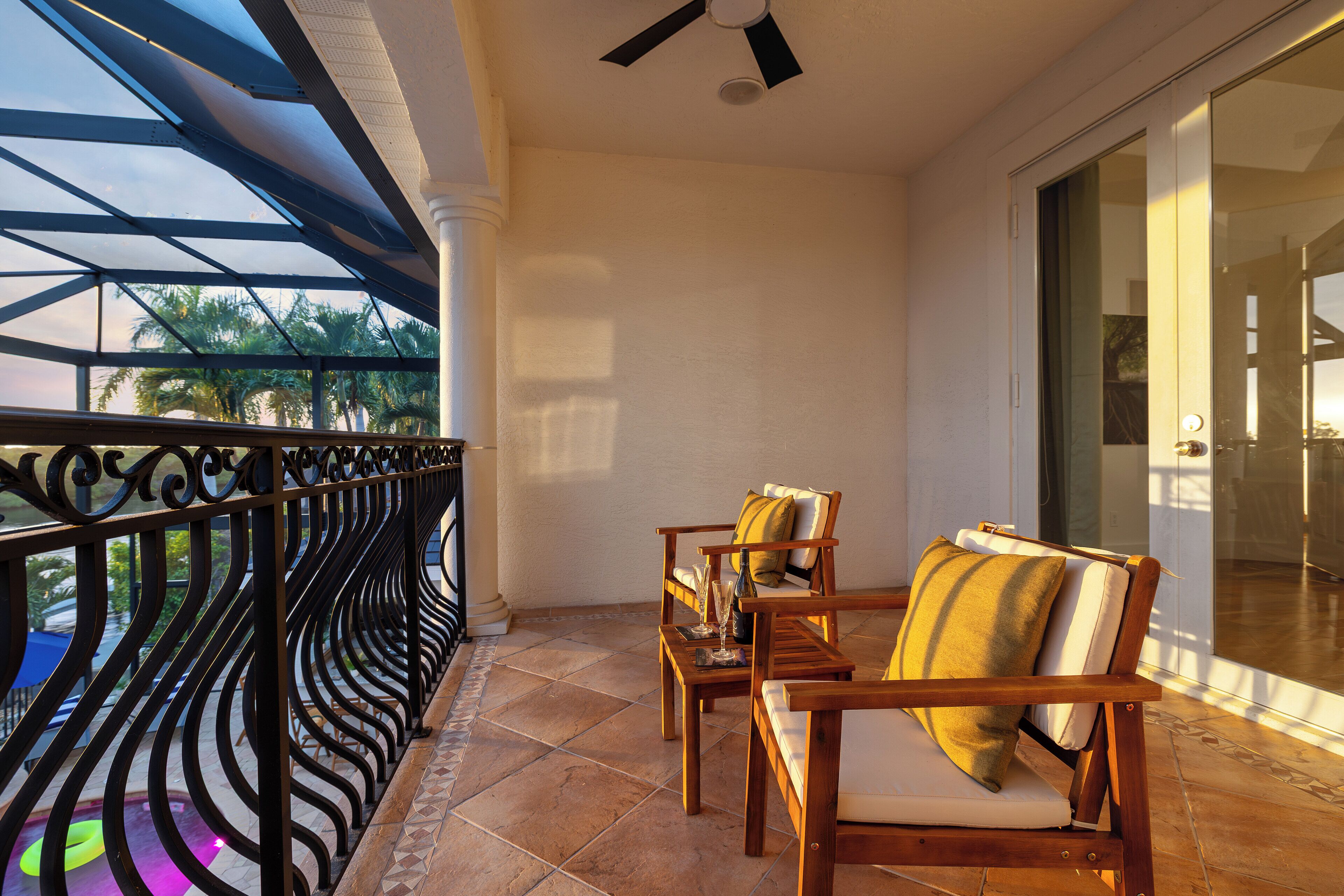 A balcony with a metal railing, two wooden chairs with cushions, and a glass door leading to an interior space.