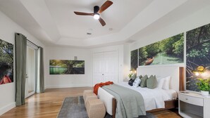 Un dormitorio con cama, ventilador de techo, ventana grande y obras de arte en las paredes.
