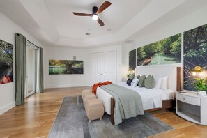 Ein Schlafzimmer mit einem Bett, einem Deckenventilator, einem großen Fenster und Kunstwerken an den Wänden.