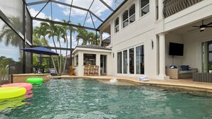 Una piscina interior con agua cristalina, rodeada por un patio cubierto con asientos y un televisor.