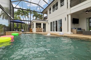 Ein überdachter Patio-Bereich mit Sitzgelegenheiten und einem Fernseher umgibt ein Hallenbad mit klarem Wasser.
