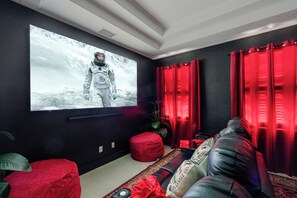 Ein Zimmer mit einem großen Flachbildfernseher an der Wand, einem roten Sofa, einem roten Hocker und einem gemusterten Teppich.