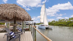 Terraza de madera con sillones de descanso y una estructura de techo de paja, con vista a aguas tranquilas y veleros.