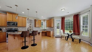 A modern kitchen with wooden cabinets, a central island with bar stools, and a dining area with a glass table and chairs. - Modern 4BR Retreat Near ATL Airport & Attractions (Atlanta)